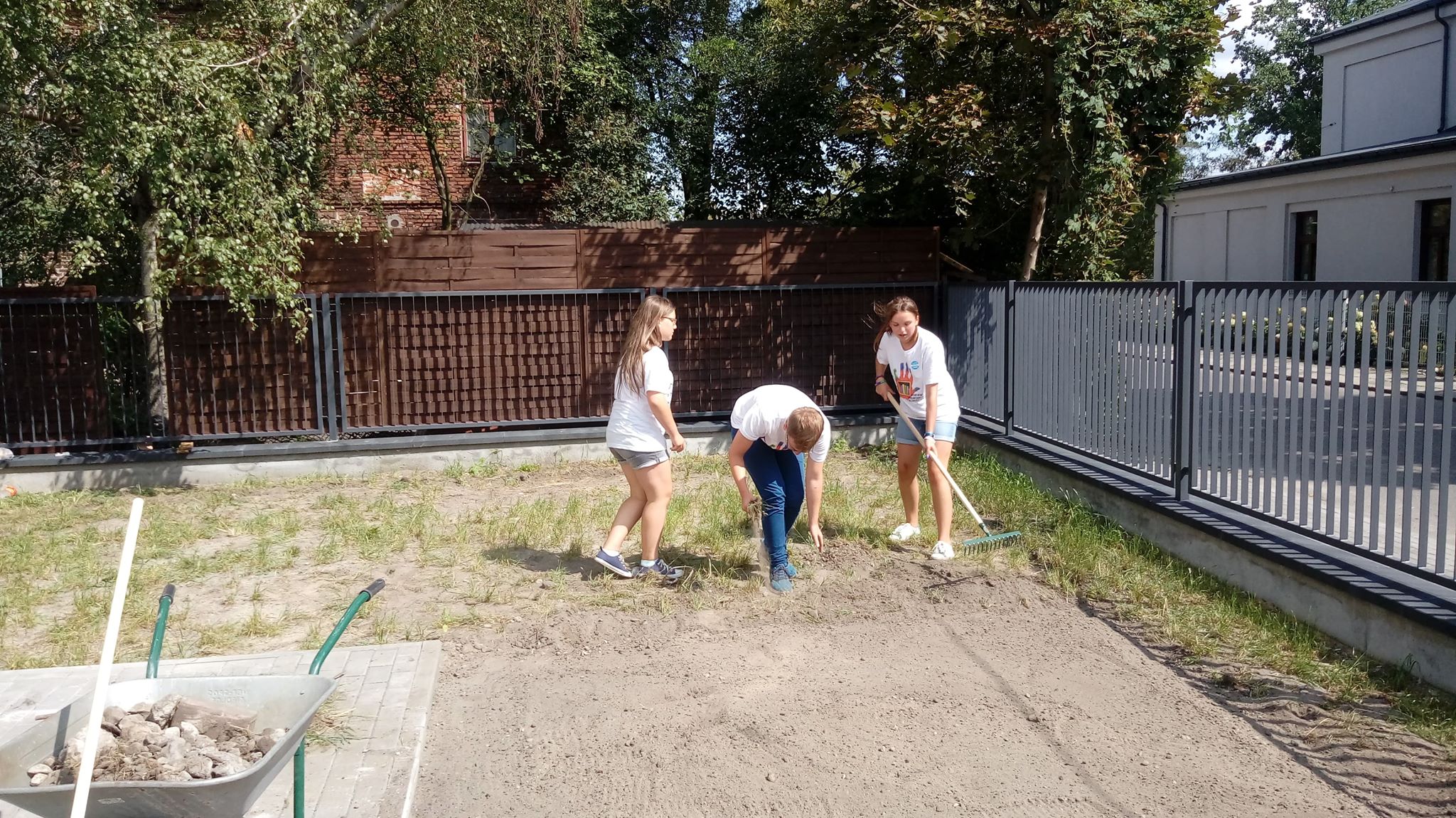 Troje młodych wolontariuszy z dzielnicy Wawer grabi trawnik na terenie biblioteki