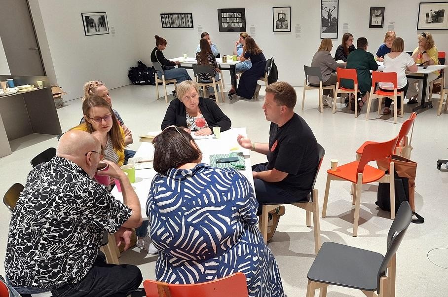 Praca warsztatowa, dyskutujący ze sobą ludzie siedzący w grupach przy stolikach