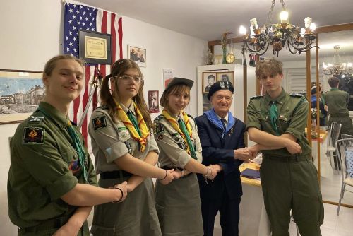 Zdjęcie grupy dwóch harcerek i dwóch harcerzy ubranych w mundury zawiązujących harcerski krąg z Powstańcem