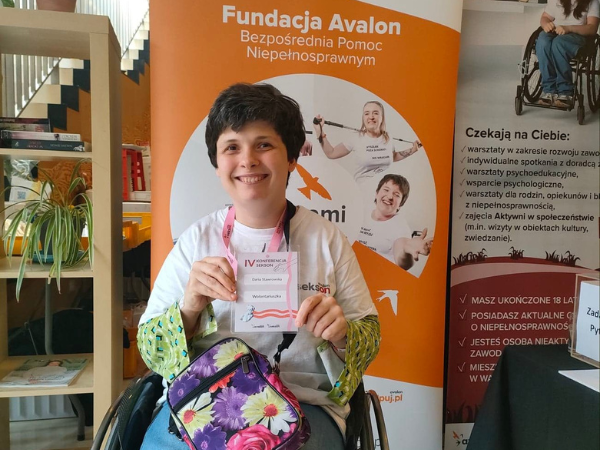 Kobieta na wózku inwalidzkim w białej koszulce z napisem "Avalon. Sekson" trzymająca identyfikator z napisem IV Konferencja Sekson. Daria Stawrowska. Wolontariuszka"