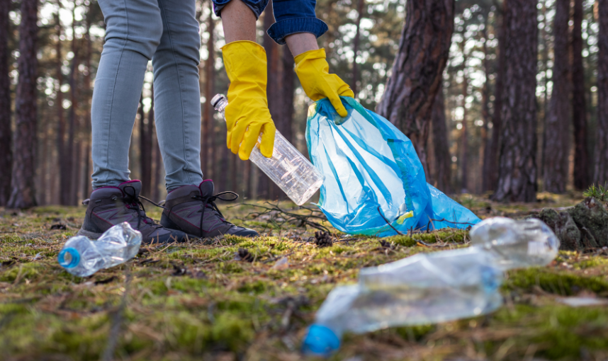 Osoba w żółtych rękawiczkach wkładająca plastikową butelkę do niebieskiego worka na śmieci