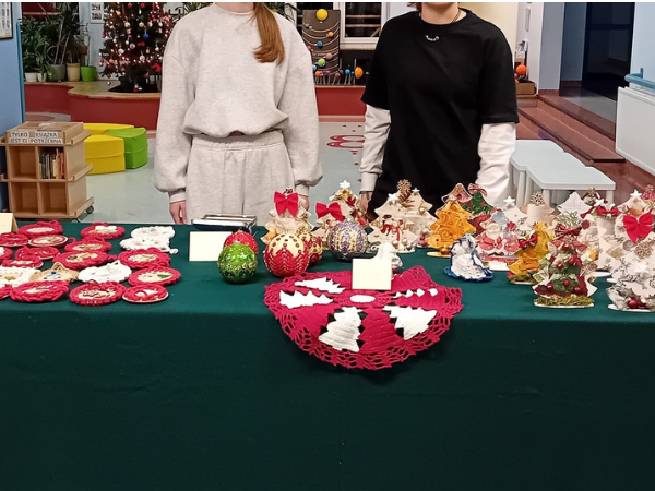 Długi stół z butelkowozielonym obrusem, na którym ułożone są różnego rodzaju ozdoby, na przykład małe obrusy, podkładki oraz małe choinki. 