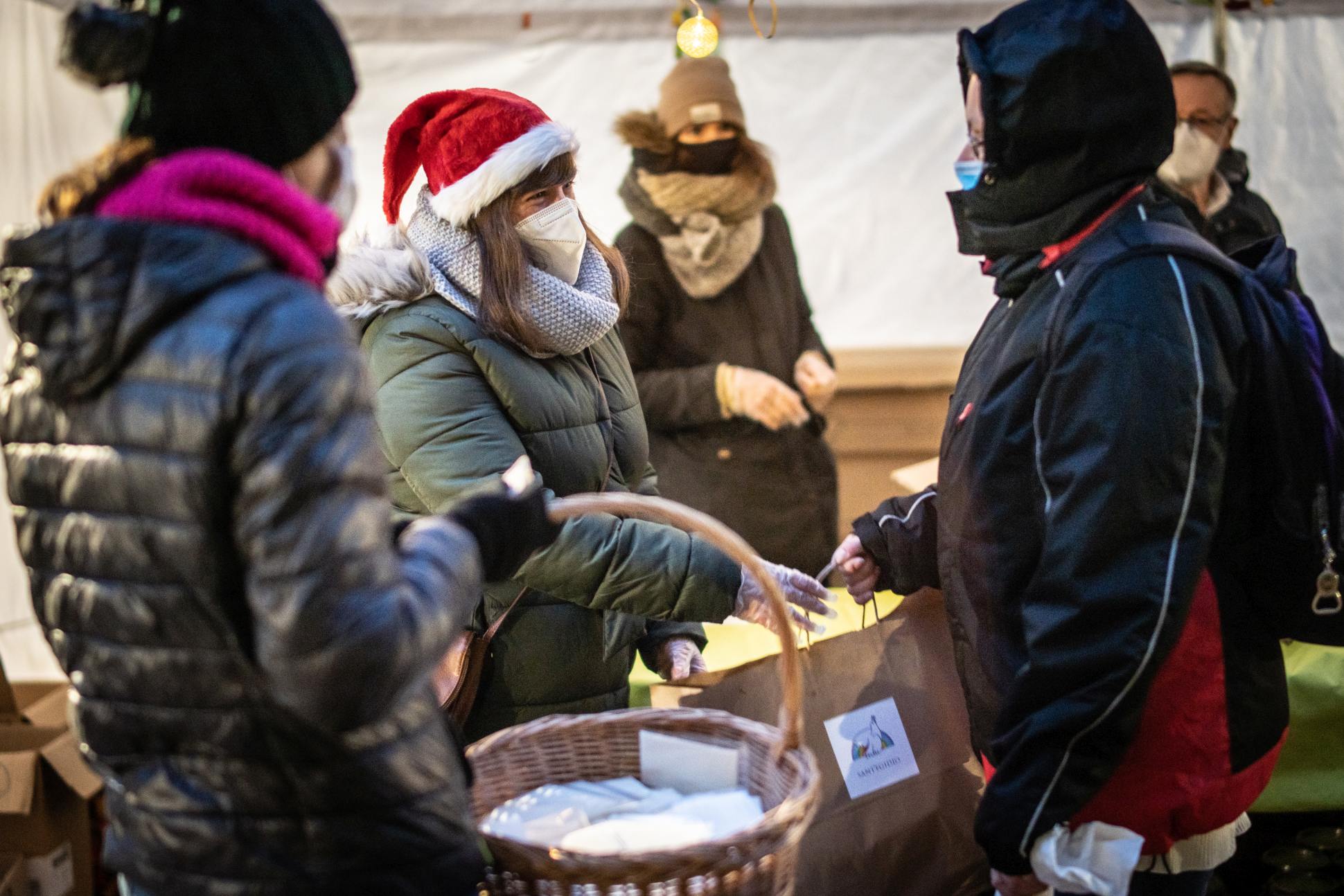 Wolontariuszka w czapce Mikołaja przekazuje torebkę z upominkiem osobie bezdomnej