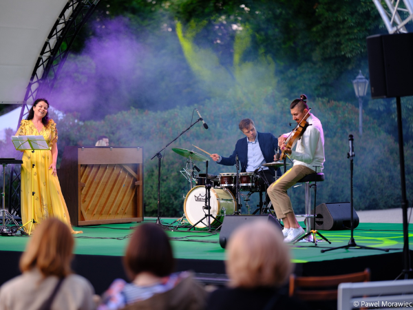 Kobieta i dwóch mężczyzn stojących na scenie i grających na instrumentach