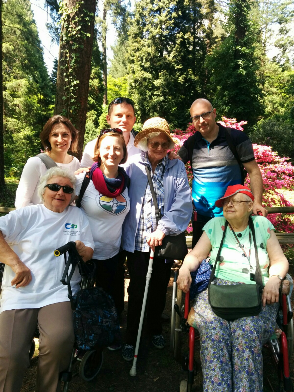Podopieczni stowarzyszenia razem z wolontariuszami na tle ogrodu w trakcie wycieczki