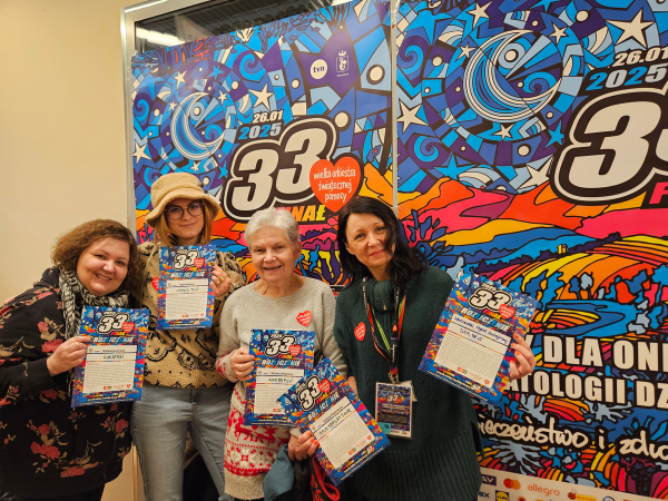 Scena na placu oświetlona na żółto i zielono. Na scenie znajdują się dwie osoby przebrane za zwierzęta. Przed sceną zgromadzony jest tłum.