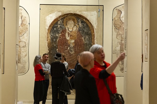 Zdjęcie wolontariuszek w Galerii Faras podczas wydarzenia Wielkie Opowiadanie, dwie wolontariuszki w czerwonych koszulkach rozmawiają ze zwiedzającymi stojąc przy płaskorzeźbach