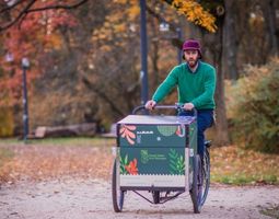 Pracownik ZZW podczas jazdy na rowerze z wózkiem w parku.