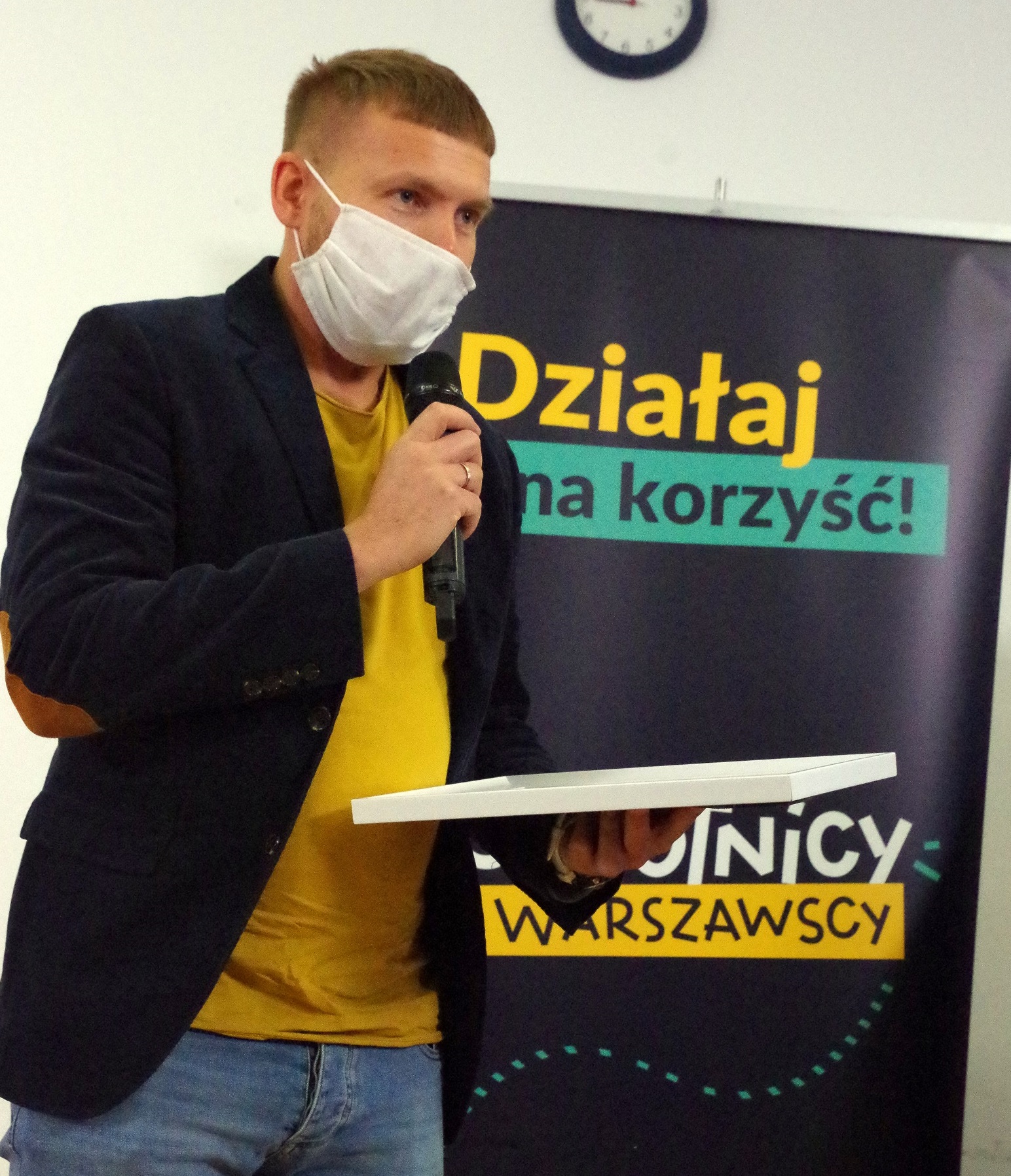 Przemysław Skwarski z dyplomem i mikrofonem w rękach na tle napisu "Działaj na korzyść" po otrzymaniu nagrody