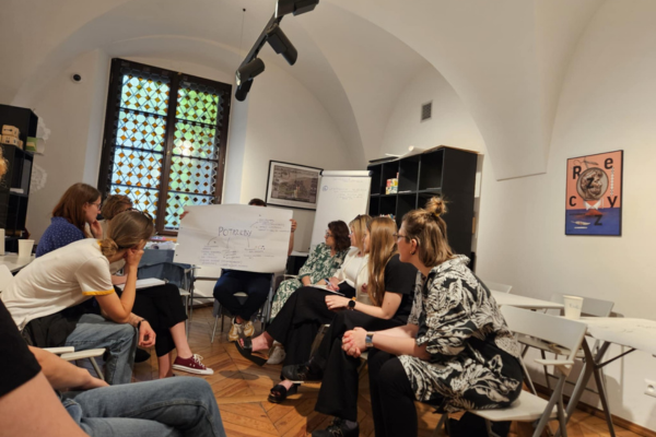 Pracownicy i pracowniczki muzeum zgromadzeni w sali Muzeum Warszawy. Na środku znajduje się flipchart, na którym wypisane są potrzeby uczestników i uczestniczek.