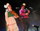 Muzykantka na skrzypcach i muzykant na dudach grają na scenie w trakcie festiwalu. Ubrani są w mazowieckie stroje ludowe i śpiewają.