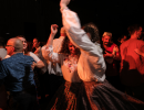 Uczestnicy wraz z wolontariuszami tańczą do muzyki festiwalowej. Ubrani w stroje ludowe. W centrum dwie tańczące muzykantki.