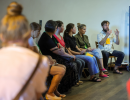 Wolontariusze i wolontariuszki siedzą w okręgu, Na środku znajduje się prowadzący warsztaty ze storytellingu, który tłumaczy coś reszcie grupy.