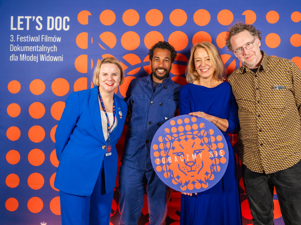 Organizatorzy i uczestnicy festiwalu Let's Doc na tle ścianki promocyjnej z logotypami festiwalu
