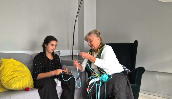 Seniorka pokazująca młodej dziewczynie technikę szydelkowania