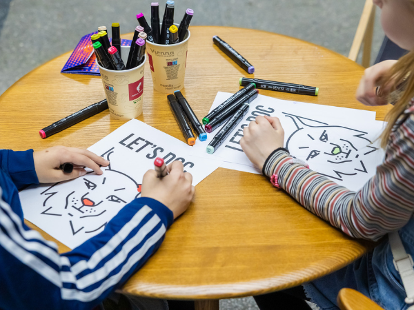 Siedzące przy stoliku dzieci kolorują logotyp festiwalu Let's Doc