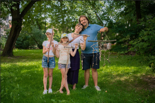Zdjęcie wykonane w parku prezentujące dwie osoby dorosłe i dwójkę dzieci trzymających dekoracje wykonane z gałęzi drzew i sznurka