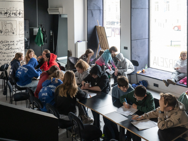 Młodzi wolontariusze i wolontariuszki uczestniczą w warsztacie, pracując w grupach przy stole w sali Centrum Kultury Filmowej im. Andrzeja Wajdy