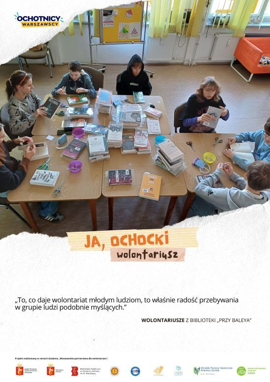 Plakat ze zdjęciem grupy młodzieży, siedzącej przy połączonych ze sobą stolikach, oprawiającej książki biblioteczne, napis "Ja, ochocki wolontariusz"