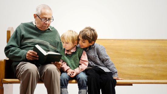 Starszy mężczyzna czyta książkę dwójce kilkuletnich chłopców