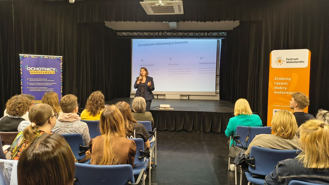 Prelegentka przemawia do uczestników i uczestniczek konferencji. W tle widoczny jest ekran, na którym wyświetlona jest prezentacja multimedialna.