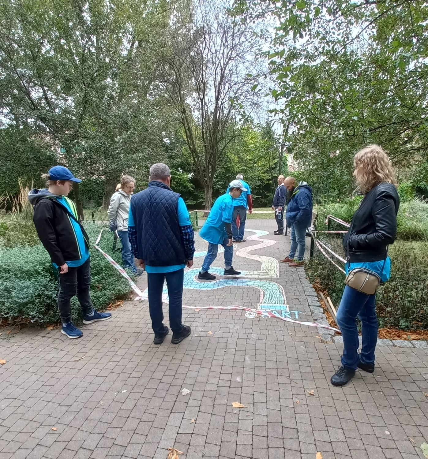 Uczestnicy "Wolontariackiego Pikniku Rodzinnego" rysują kredą tor kapslowy na chodniku 