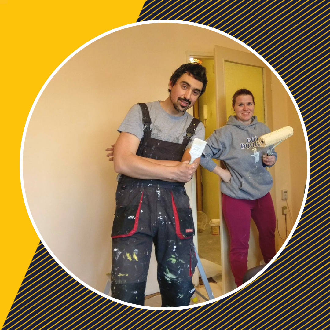 Wolontariuszka i wolontariusz podczas remontu mieszkania. Wolontariuszka trzyma w ręku wałek malarski, a wolontariusz pędzel. 