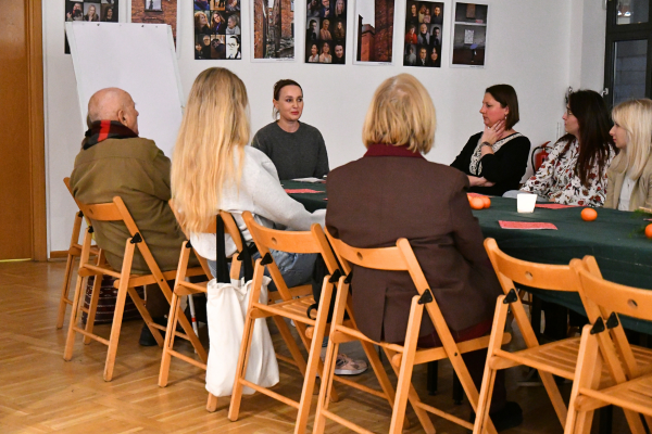 Uczestniczki i uczestnicy empatycznego warsztatu zgromadzeni przy jednym stole. Na środku siedzi osoba prowadząca warsztat.