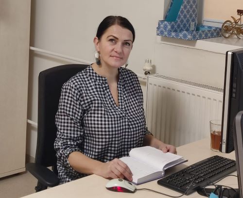 Zdjęcie Agnieszki Jaćwiąg siedzącej przy biurku, przy komputerze, przeglądającej notatnik/kalendarz