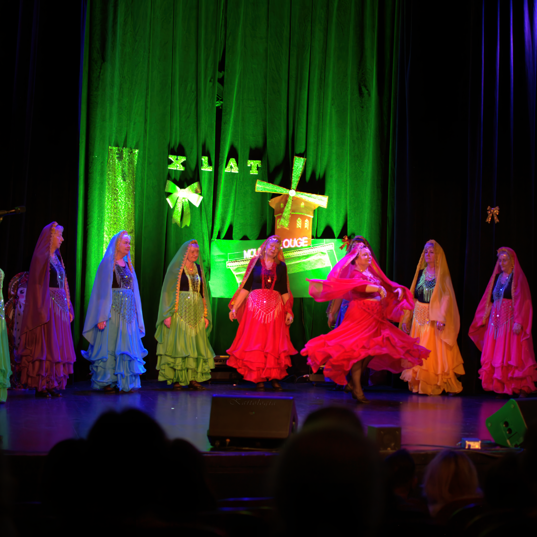 Tancerki w sukniach podczas tańca na scenie widowiskowej. W tle wiatrak i napis: X lat.