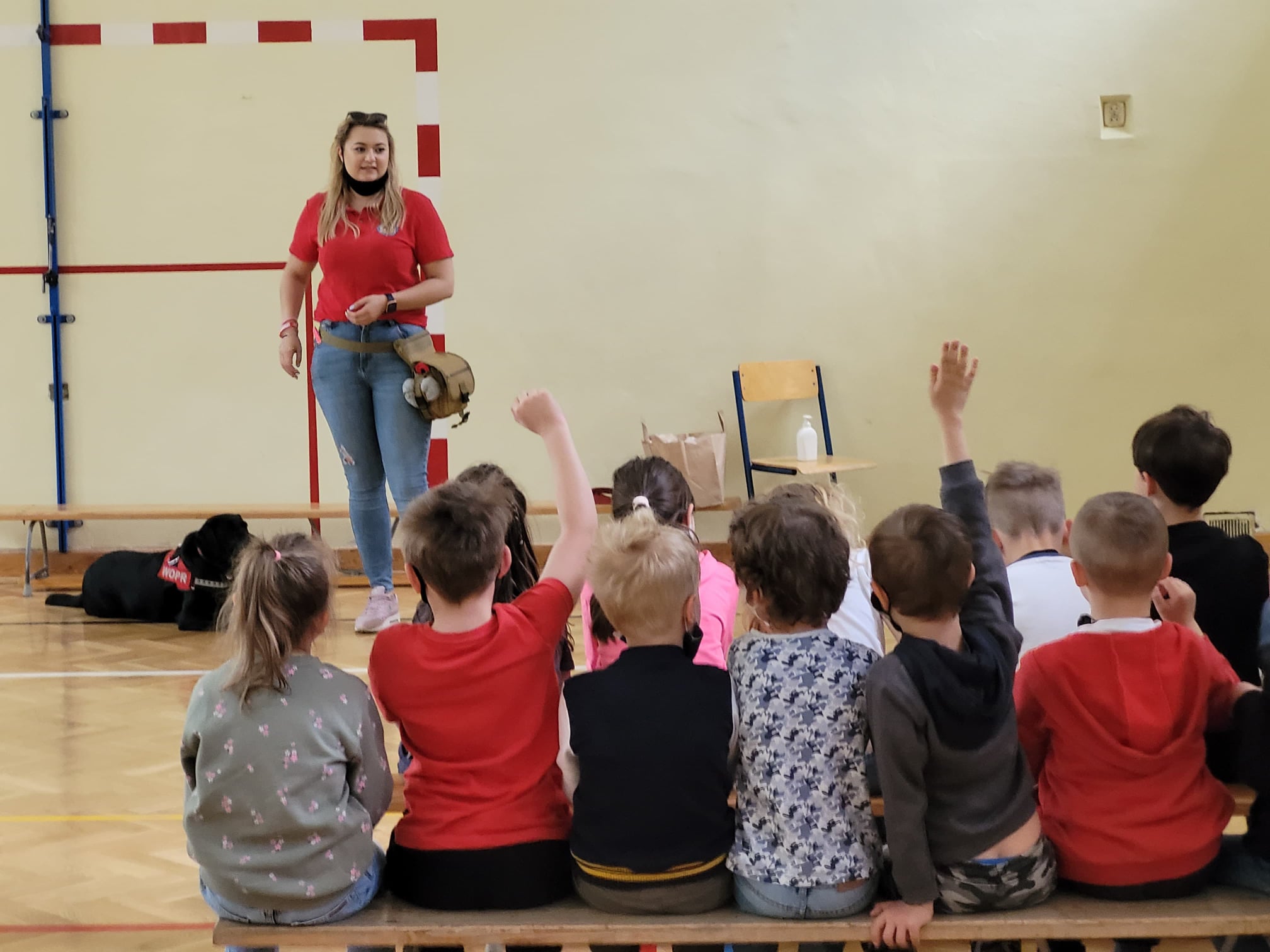 Dzieci w sali gimnastycznej słuchające członkini WOPR. Pogadanka w szkole