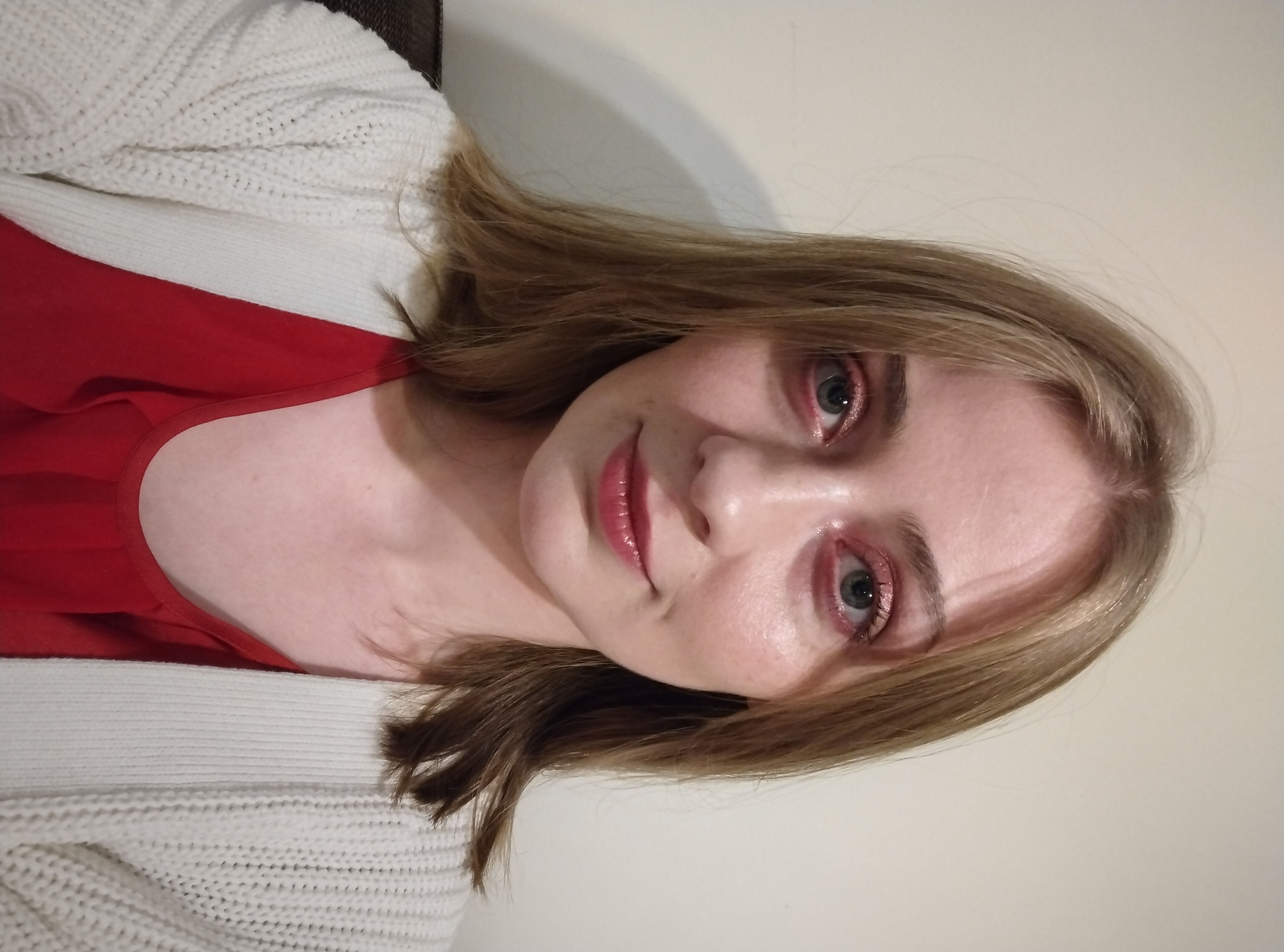 Zdjęcie portretowe przedstawiające wolontariuszkę. Ma proste blond włosy do ramion i czerwony brokatowy cień do powiek. Jest ubrana w czerwoną koszulę i kremowy kardigan.