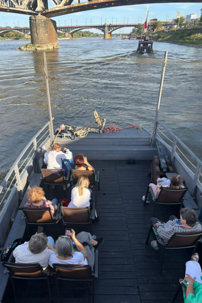 Zdjęcie ze spływu integracyjnego wolontariuszy z podopiecznymi, widok z górnego pokładu. Osoby siedzą na barce na krzesłach.