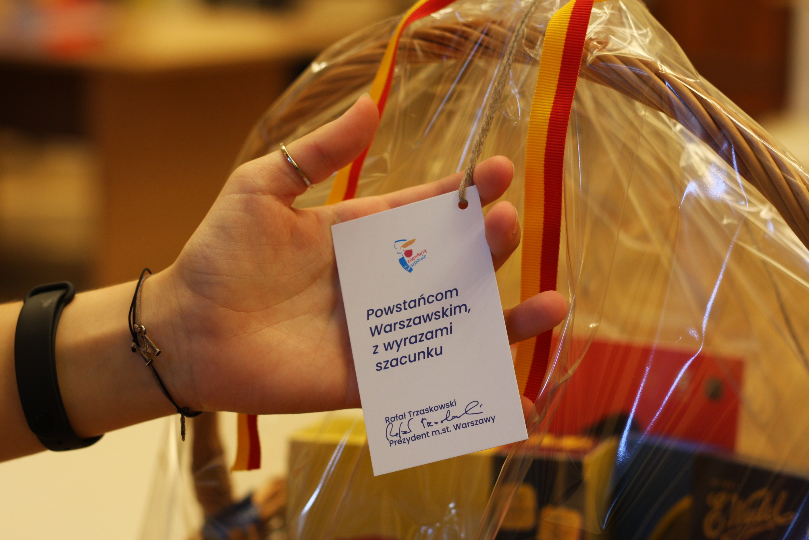 Dłoń podtrzymująca kartkę z życzeniami od Prezydenta Warszawy dla Powstańca