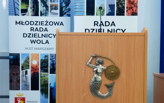 Mównica z warszawską syrenką, w tle roll-upy Mlodziezowej rady dzielnicy Wola oraz Rady dzielnicy Wola